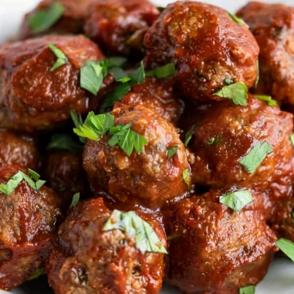 Close-up of vegan meatballs coated in a rich, dark sauce and garnished with fresh parsley.